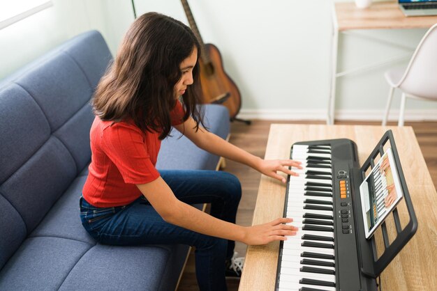 Jolie préadolescente suivant les instructions de son professeur de musique et apprenant à jouer du piano. Fille hispanique prenant des cours d'art lors d'un appel vidéo en ligne