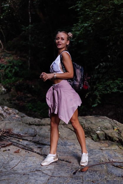 Photo gratuite jolie touriste en haut court blanc avec sac à dos se dresse sur un rocher en forêt