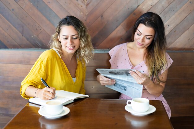 Jolies femmes buvant du café et lisant un journal au café