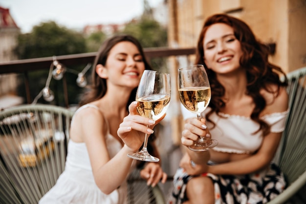 De jolies femmes profitent d'une bonne journée avec du vin sur la terrasse De jolies filles de bonne humeur s'amusent et posent pour la caméra