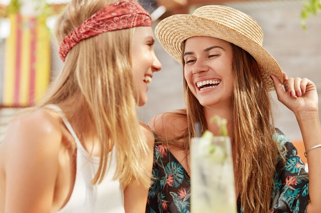 les jolies femmes recréent ensemble au café, boivent des cocktails frais. Les femelles adorables détendues se détendent pendant les vacances d'été.