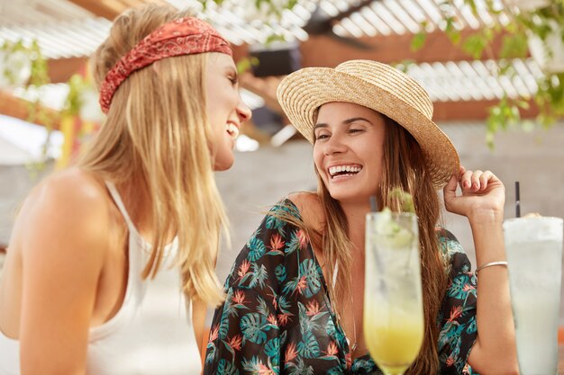 les jolies femmes recréent ensemble au café, boivent des cocktails frais. Les femelles adorables détendues se détendent pendant les vacances d'été.