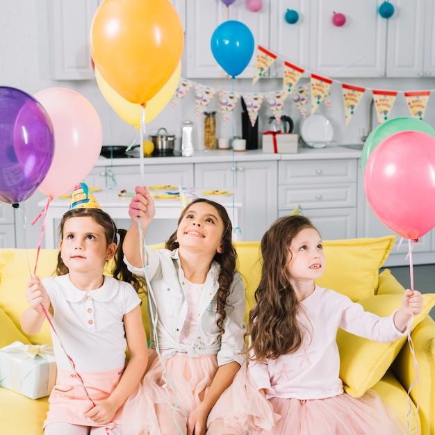 Jolies filles assises sur le canapé tenant des ballons colorés