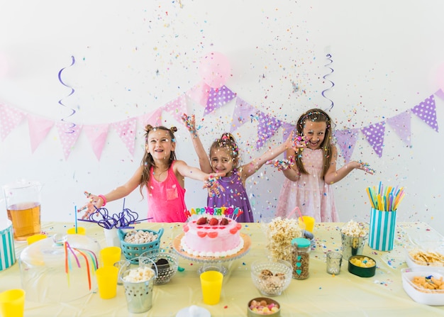 Jolies filles profitant d&#39;une fête d&#39;anniversaire à la maison avec une variété de nourriture et de jus sur la table