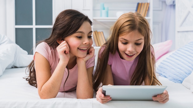 Jolies filles souriantes allongé sur le lit en regardant une tablette numérique