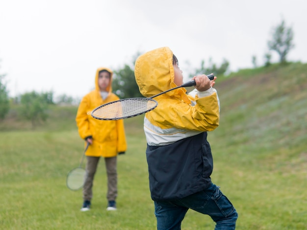 Jolis garçons en imperméable jouant au badminton