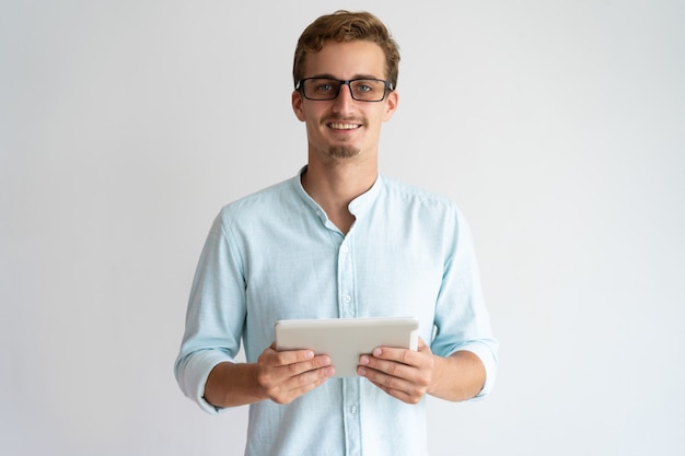 Jolly a excité le beau spécialiste masculin travaillant avec la tablette et regardant la caméra.