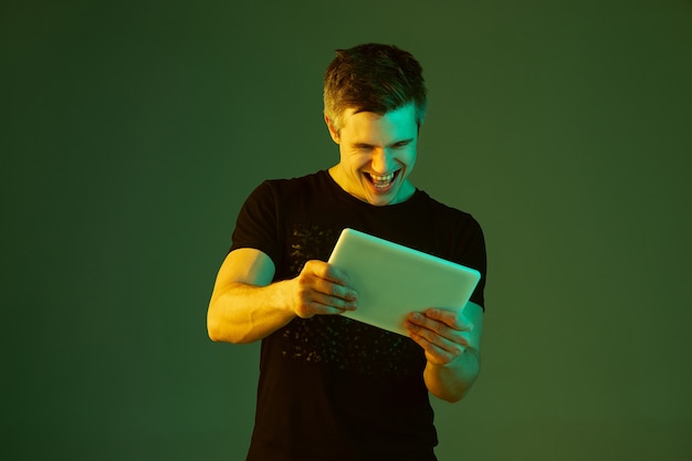 Jouer avec une tablette. Portrait de l'homme caucasien isolé sur fond vert en néon.