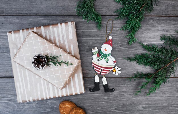 Jouet bonhomme de neige près de cadeaux dans des emballages avec accroche, brindilles et biscuits