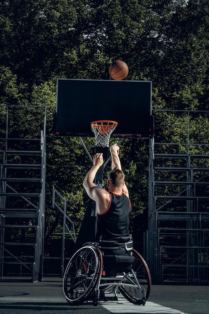 Photo gratuite un joueur de basket-ball infirme en fauteuil roulant joue au basket-ball sur un terrain en plein air.
