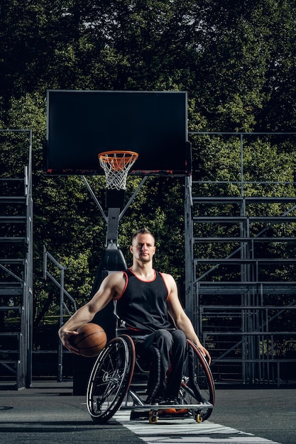 Joueur de basket-ball infirme en fauteuil roulant tenant le ballon sur un terrain découvert.