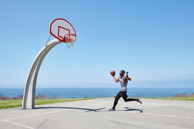 Joueur de basket-ball qui court au bord de l'océan avec caméra selfie