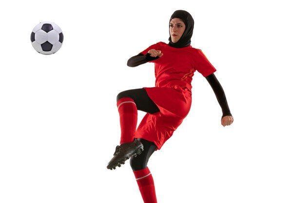 Joueur de football ou de football féminin arabe isolé sur fond de studio blanc. Jeune femme botter le ballon, s'entraîner, pratiquer en mouvement et en action.