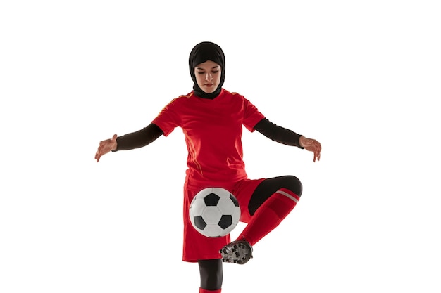 Joueur de football ou de football féminin arabe isolé sur fond de studio blanc. Jeune femme botter le ballon, s'entraîner, pratiquer en mouvement et en action.