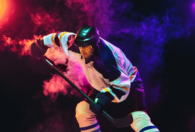 Joueur de hockey masculin avec le bâton sur un court de glace et un mur de couleur néon foncé