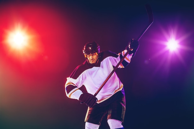 Joueur de hockey masculin avec le bâton sur un court de glace et un mur de couleur néon foncé