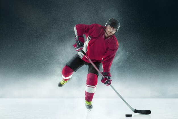 Joueur de hockey masculin avec le bâton sur un court de glace et un mur sombre