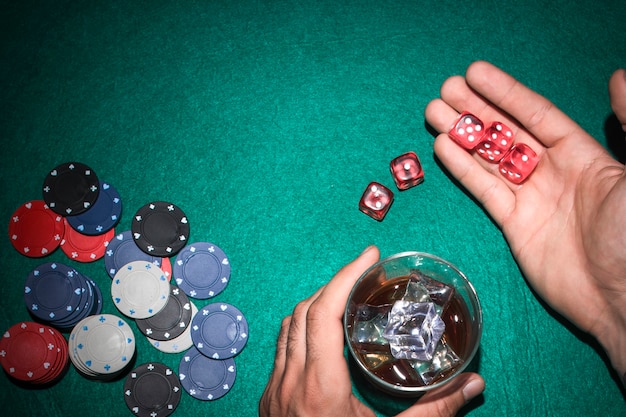 Un joueur de poker montrant des dés rouges avec un verre de whisky sur une table de poker