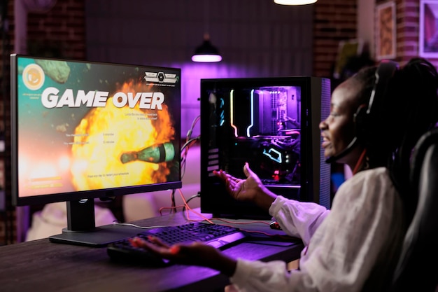 Photo gratuite le joueur se sent contrarié après avoir perdu sa mission de jeu vidéo d'action solo, étant déjoué par ses ennemis. une femme afro-américaine confuse après avoir vu un jeu sur écran sur un ordinateur de jeu