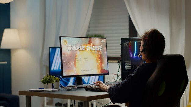 Joueuse pro furieuse avec casque perdant un jeu vidéo de tir spatial avec de nouveaux graphismes pendant le championnat de jeu jouant à domicile sur un ordinateur personnel puissant RVB, se produisant lors d'un tournoi d'esports