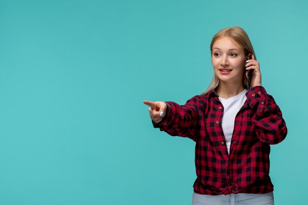 Journée internationale des étudiants jeune fille mignonne en chemise à carreaux rouge pointant vers quelqu'un avec le téléphone