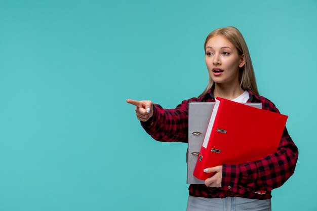 Journée internationale des étudiants jolie fille blonde en chemise à carreaux rouge pointant vers l'avant avec des dossiers de fichiers