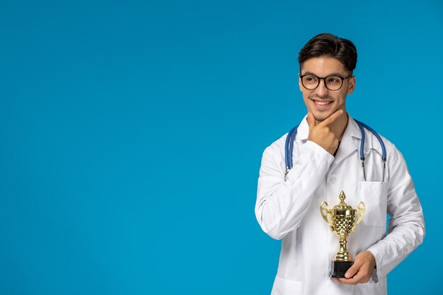 Journée des médecins beau mec mignon brune en blouse médicale souriant tenant le trophée