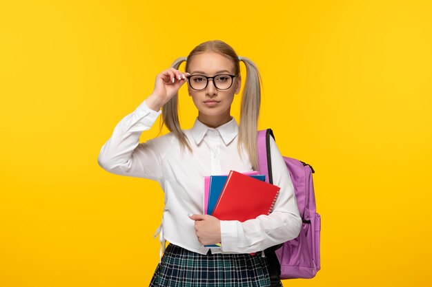 Journée mondiale du livre écolière blonde sérieuse avec des queues de cheval portant un sac à dos rose et des lunettes