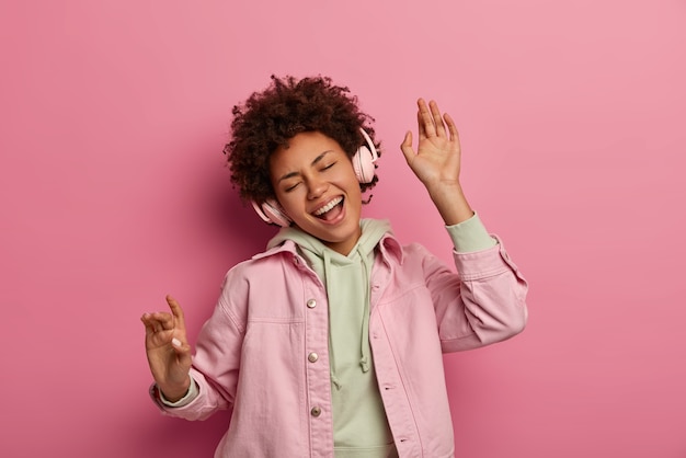 Joyeuse adolescente aux cheveux bouclés danse sans soucis écoute piste audio dans les écouteurs