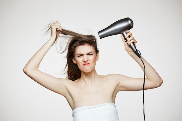 Joyeuse belle femme en serviette souriant rire en chantant avec sèche-cheveux faisant la grimace. Spa de beauté et cosmétologie.