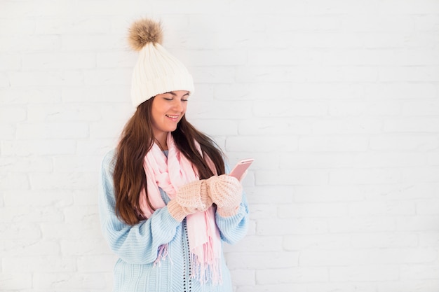 Joyeuse dame en mitaines, bonnet et écharpe avec smartphone