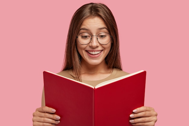 Joyeuse écolière tient un manuel, lit un livre intéressant