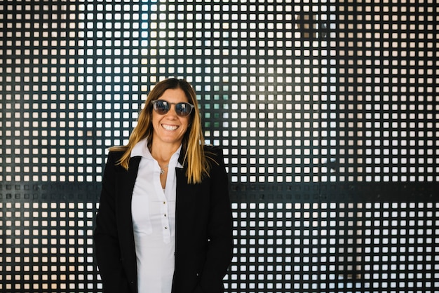 Joyeuse élégante jeune femme avec des lunettes de soleil près de clôture