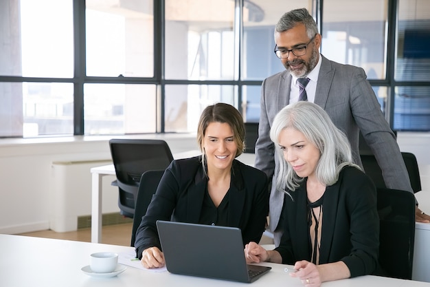 Joyeuse équipe commerciale regardant la présentation sur ordinateur portable, assis sur le lieu de travail, regardant l'affichage et souriant. Copiez l'espace. Concept de réunion d'affaires