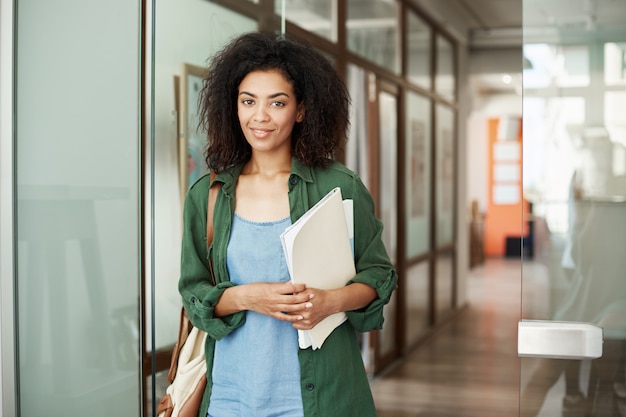 Joyeuse étudiante africaine belle femme souriante tenant des livres à l'université. Concept de l'éducation.