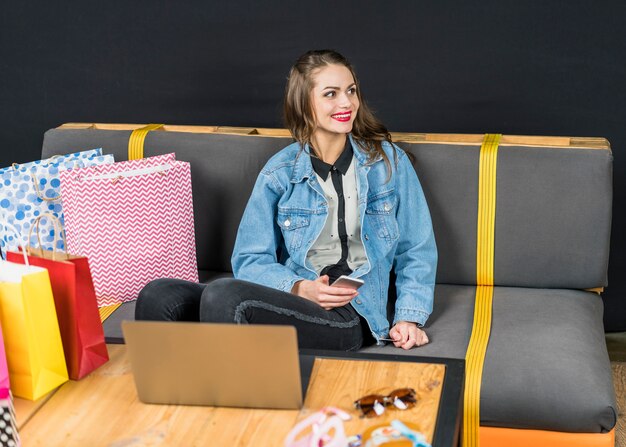 Joyeuse femme assise sur un canapé avec des sacs colorés à la maison