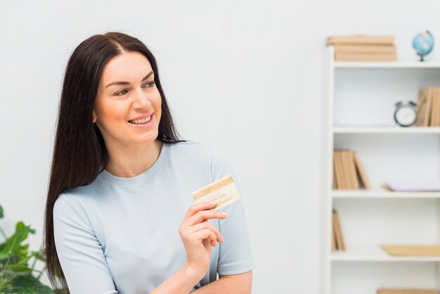 Joyeuse femme en bleu debout avec carte de crédit au bureau