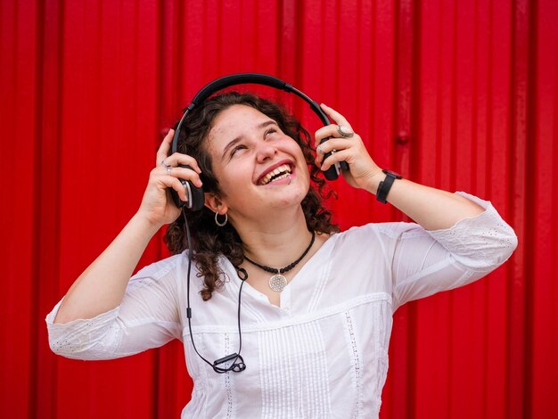 Joyeuse femme caucasienne écoutant de la musique avec des écouteurs sur une scène rouge