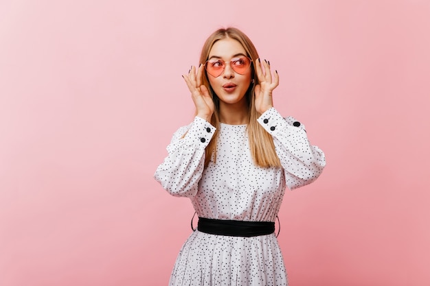 Joyeuse femme européenne à lunettes élégantes posant avec plaisir. Portrait intérieur du modèle féminin extatique en robe blanche.