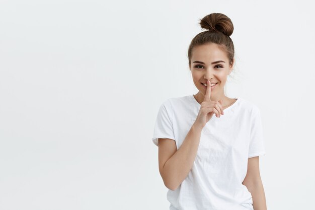 Joyeuse femme européenne à la mode souriant tout en montrant le geste chut avec l'index sur les lèvres