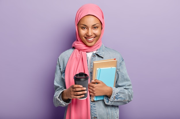 Photo gratuite joyeuse femme musulmane en hijab rose, manteau en jean, porte un portefeuille