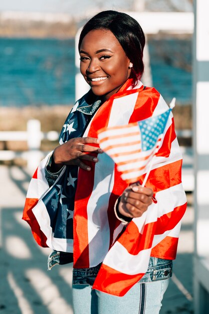 Joyeuse femme noire avec des drapeaux, debout sur la plage