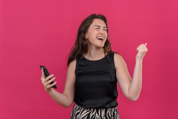 Joyeuse femme portant un maillot noir écouter de la musique à partir du téléphone sur le mur rose