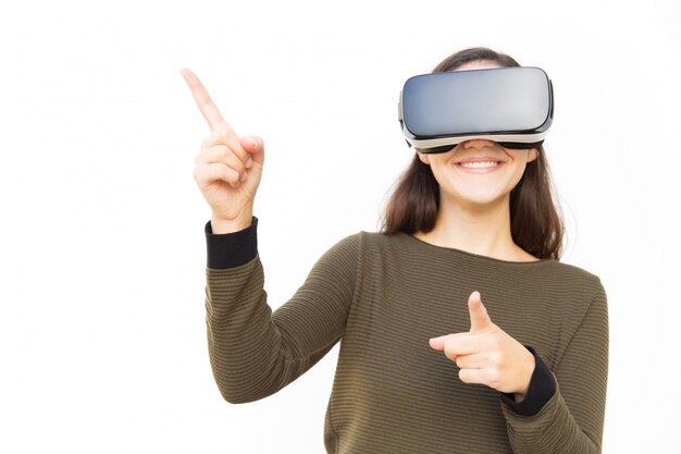 Joyeuse femme positive dans le casque VR pointant sur l'espace de copie