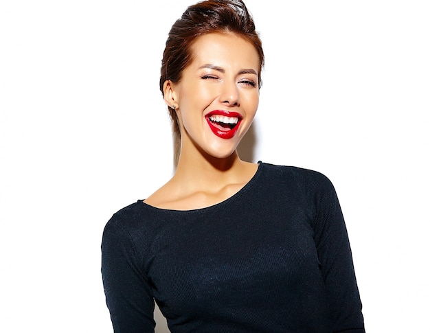 Joyeuse femme souriante de mode de clin de œil devient fou dans des vêtements noirs décontractés avec des lèvres rouges sur le mur blanc
