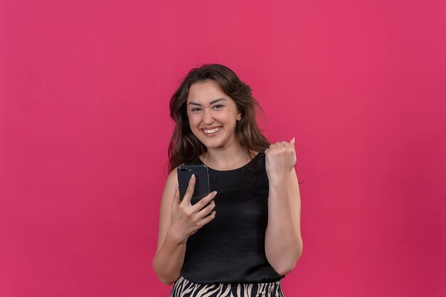 Joyeuse femme vêtue d'un maillot noir tenant un téléphone sur un mur rose