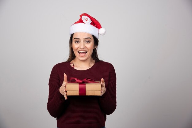 Joyeuse fille en bonnet de Noel tenant une boîte-cadeau avec bonheur.