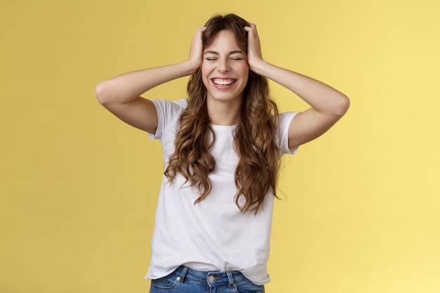 Joyeuse fille enthousiaste et enthousiaste reçoit une opportunité incroyable incroyable de voyager des vacances d'été à l'étranger attraper la tête fermer les yeux souriant joyeusement triomphant sur fond jaune optimiste