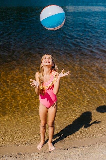 Joyeuse fille jetant un ballon de plage debout contre la mer