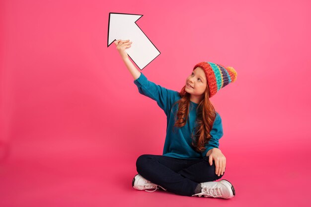 Joyeuse fille levant et tenant la flèche vers le haut isolé